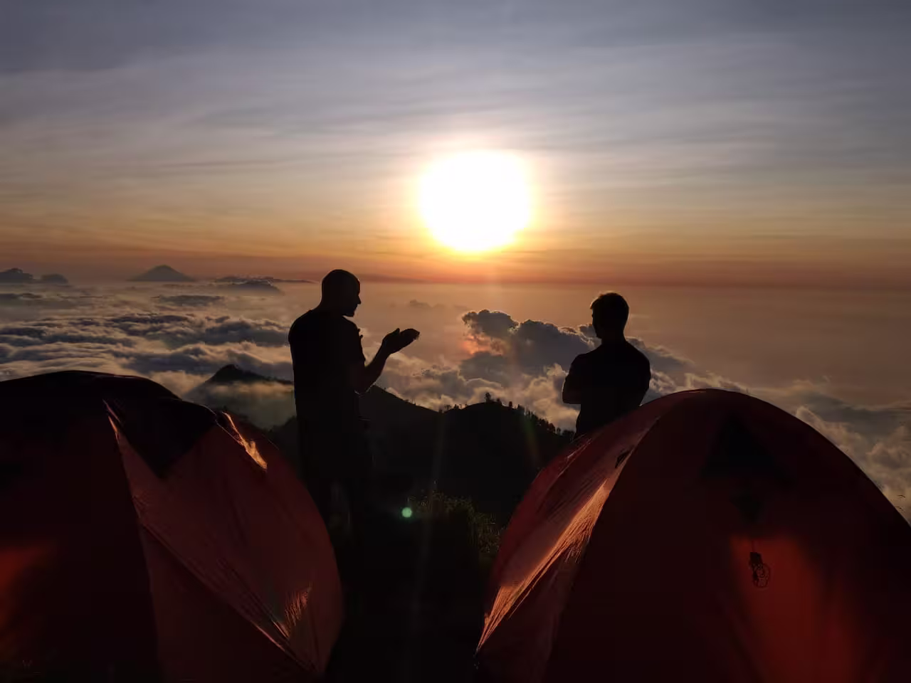 Two trekkers standing by their campsite tents at sunrise overlooking the clouds on a go2rinjani trek