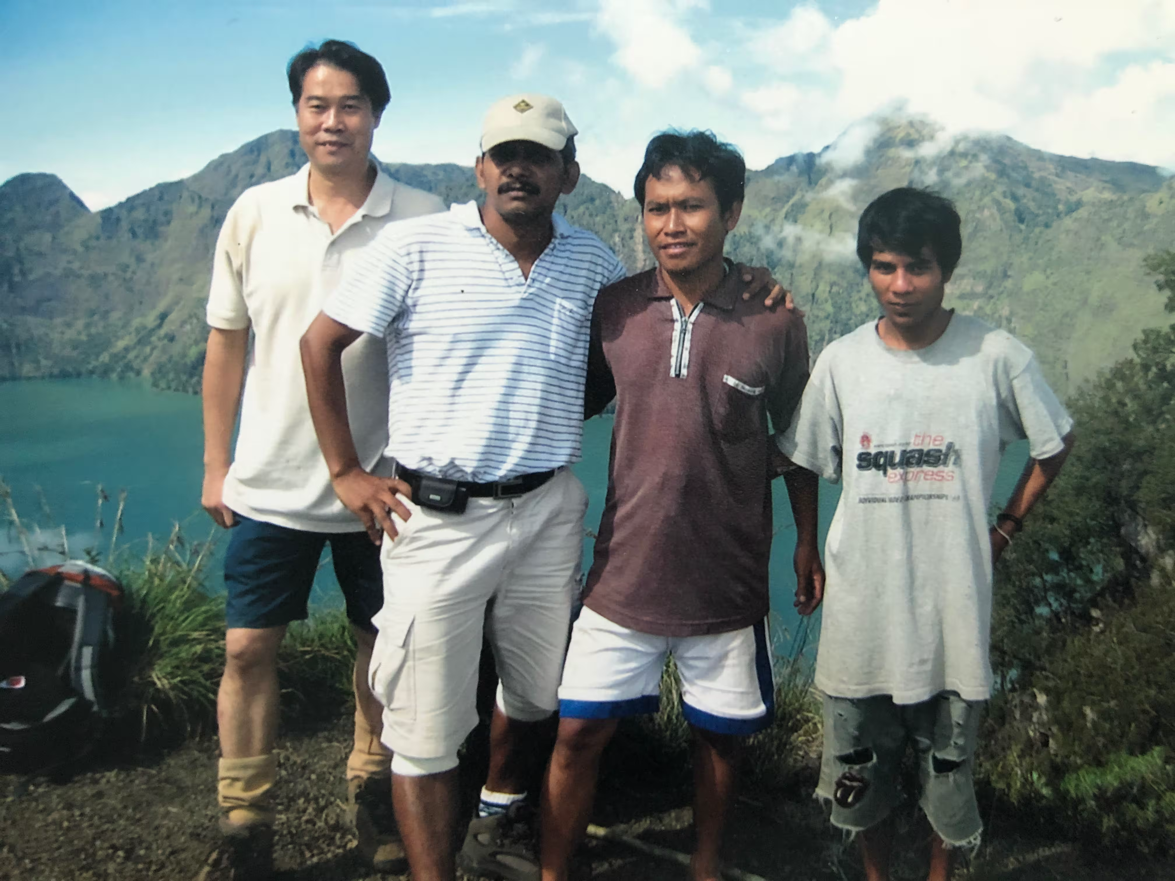 Four local guides and hikers posing together on the crater rim overlooking the turquoise Segara Anak lake on a trek organized by go2rinjani