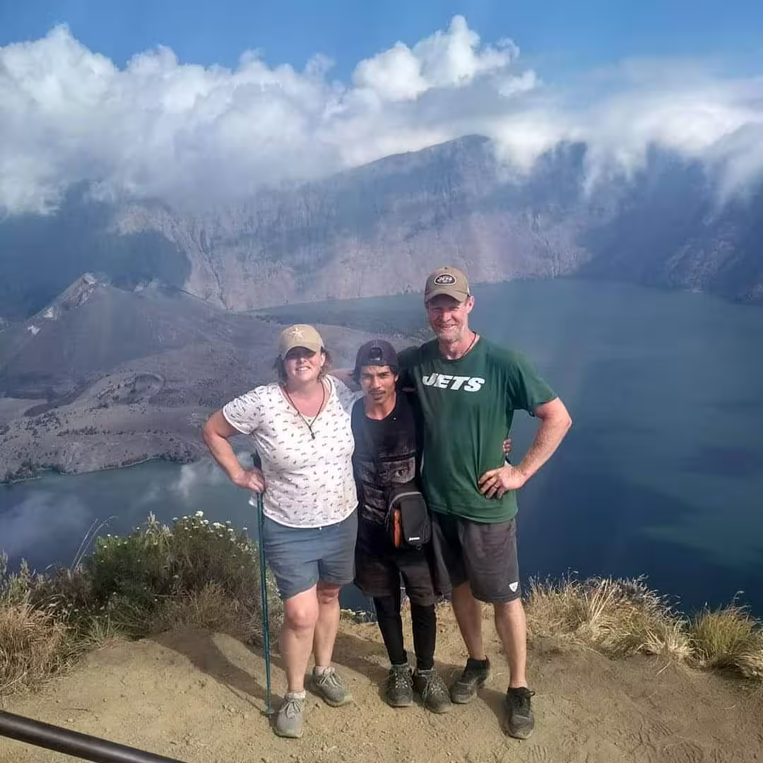 A couple and their go2rinjani guide posing on the Rinjani crater rim with Segara Anak lake behind them