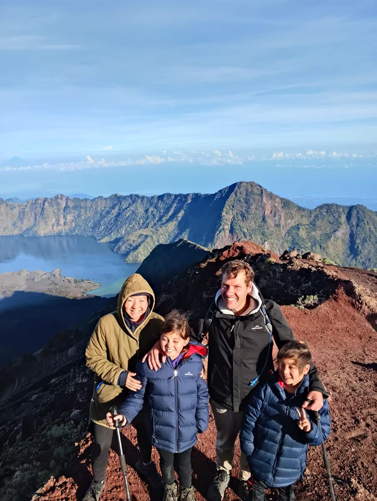 A family of four posing on the volcanic slope near the summit of Mount Rinjani during a trek guided by go2rinjani