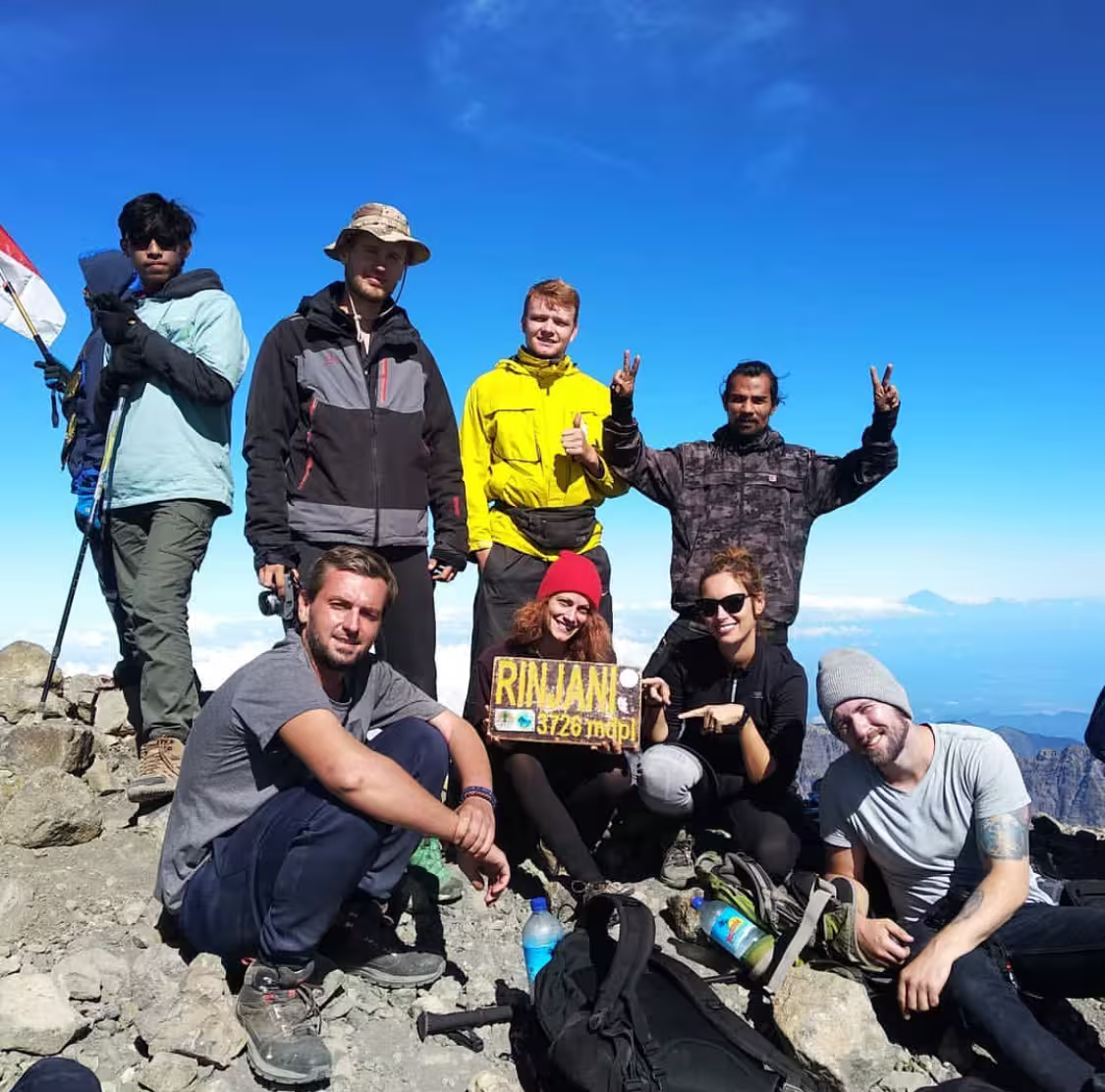 A group of happy trekkers posing with the Rinjani 3,726m summit sign during a guided climb with go2rinjani