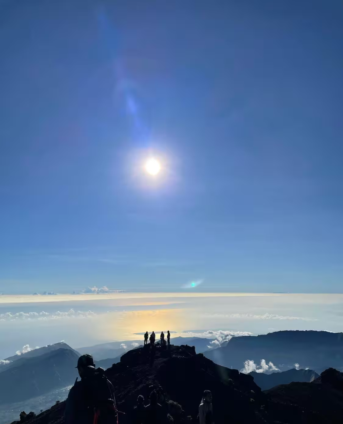Group of trekkers silhouetted on the Mount Rinjani summit with the morning sun and a sea of clouds stretching to the horizon