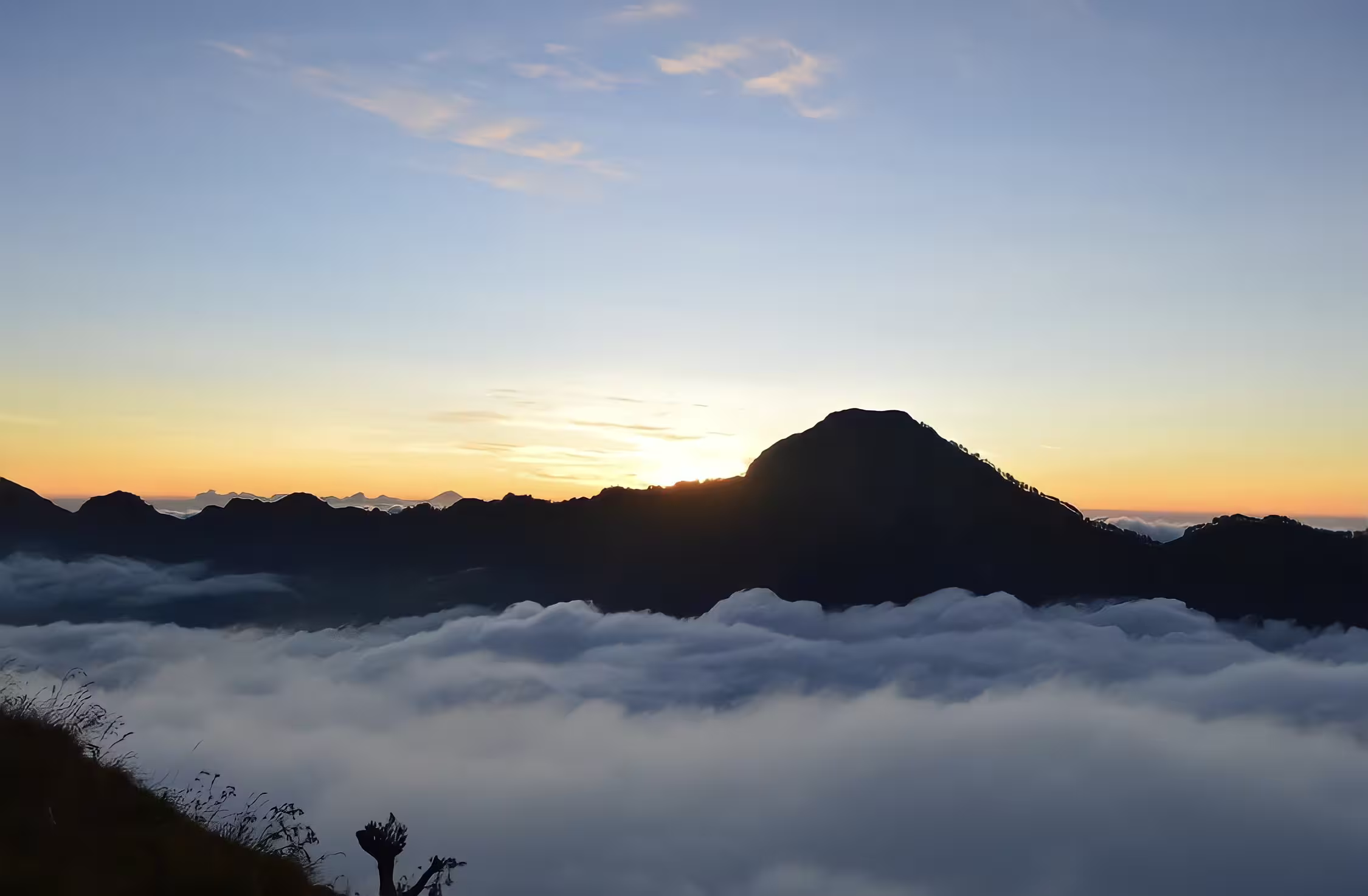 Sunrise behind the silhouetted Rinjani crater rim with a thick sea of clouds filling the caldera, a breathtaking sight on a Mount Rinjani trek