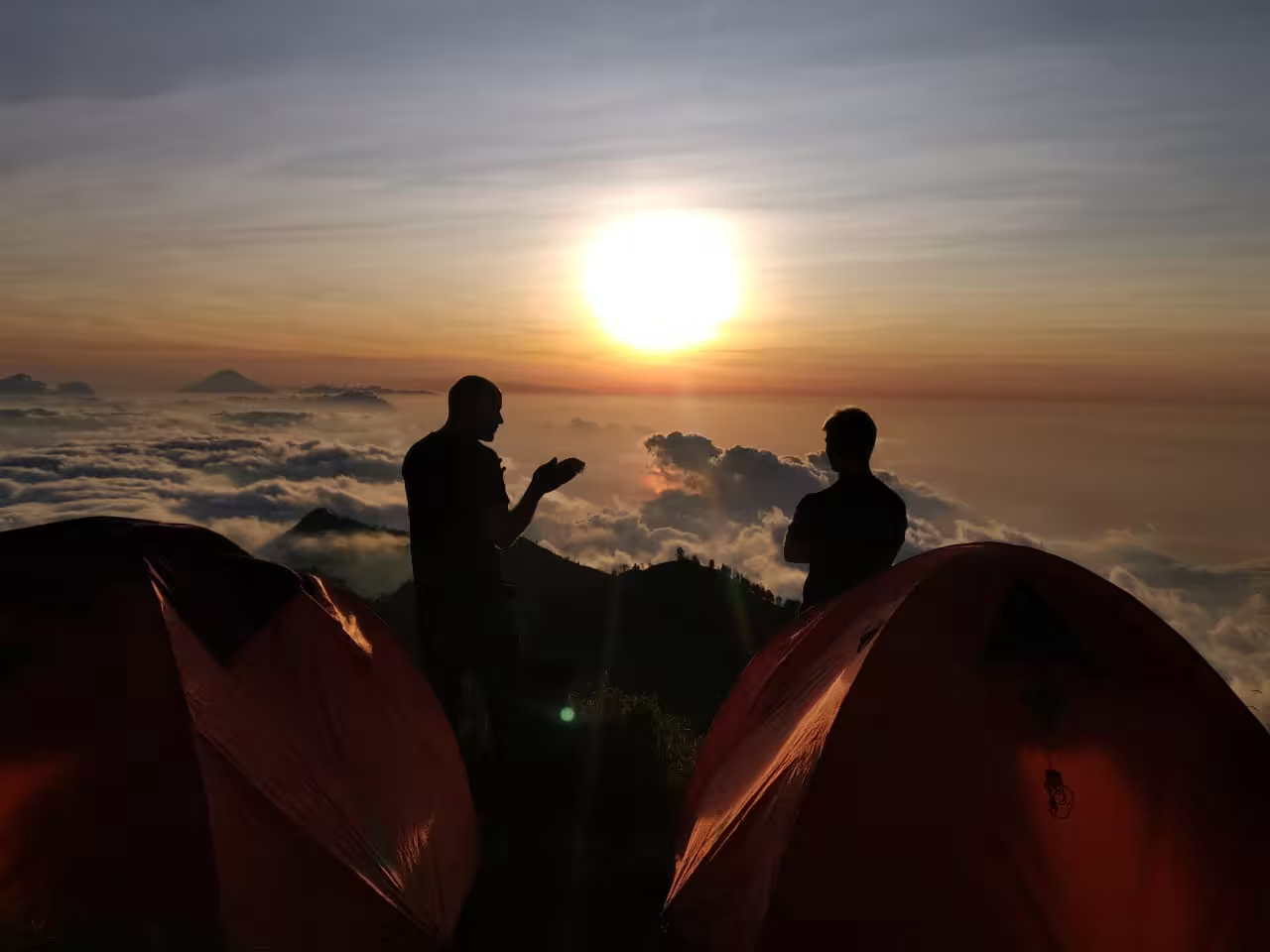 Two trekkers standing by their campsite tents at sunrise overlooking the clouds on a go2rinjani trek