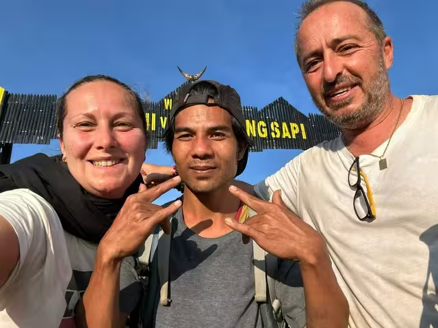 A couple taking a friendly selfie with their local guide at a trail checkpoint during a go2rinjani trek