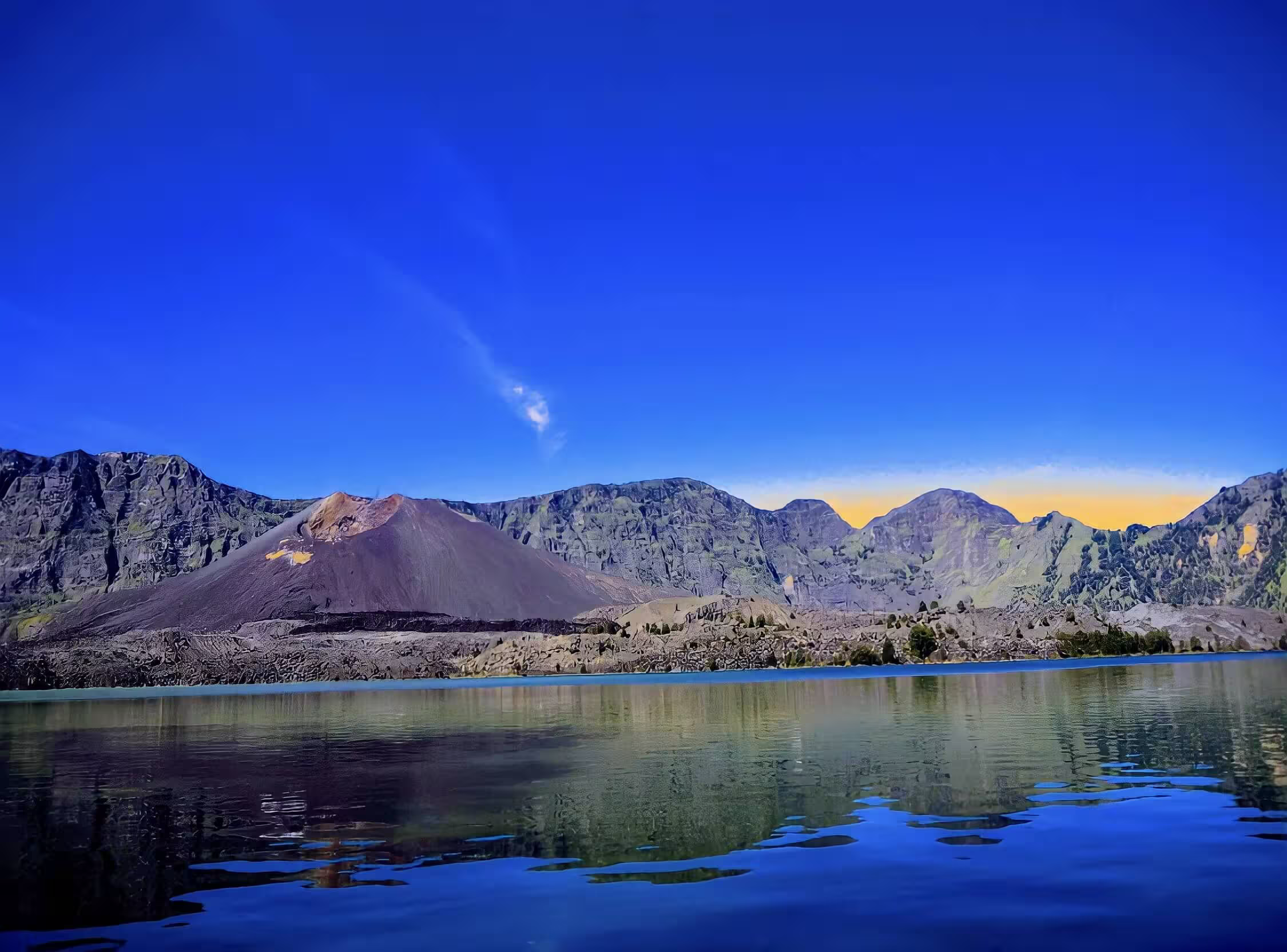 Segara Anak crater lake reflecting the Barujari volcano cone and Rinjani caldera walls at golden hour, a highlight of Mount Rinjani tour packages