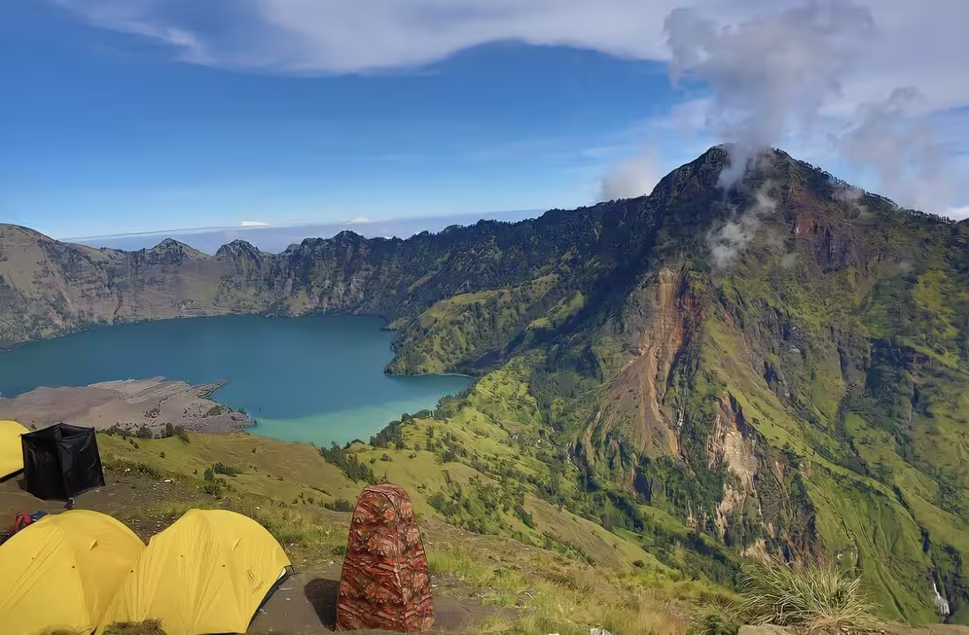 Yellow camping tents perched on the Senaru crater rim overlooking the turquoise Segara Anak lake and steaming volcanic cliffs