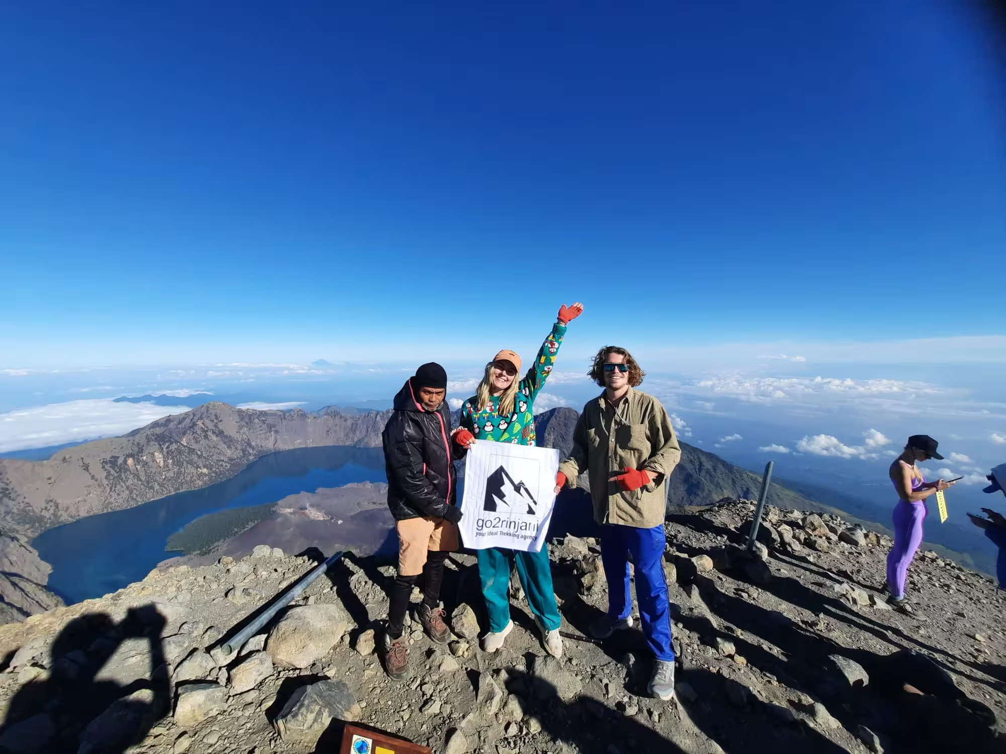 Trekkers proudly holding the go2rinjani flag at the summit of Mount Rinjani, 3,726 meters above sea level
