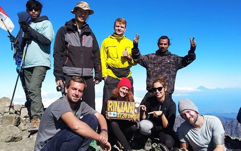 A cheerful group poses for a photo on Mount Rinjani's summit, showcasing their adventure and the beautiful landscape A cheerful group poses for a photo on Mount Rinjani's summit, showcasing their adventure and the beautiful landscape