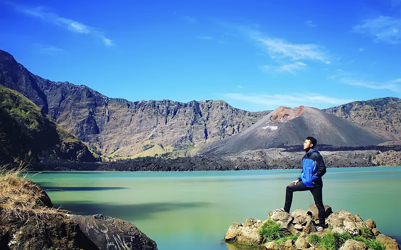 A hiker overlooks Segara Anak Lake from a rock, enjoying the view during a 3D2N trek on Mount Rinjani's Senaru route A hiker overlooks Segara Anak Lake from a rock, enjoying the view during a 3D2N trek on Mount Rinjani's Senaru route