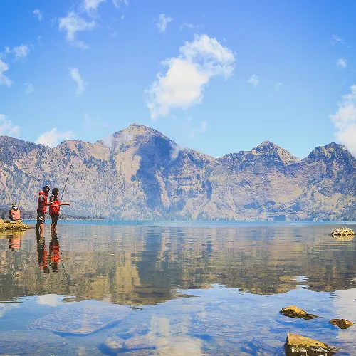 Two people stand by Segara Anak Lake, with stunning mountains in the background during a Mount Rinjani trek Two people stand by Segara Anak Lake, with stunning mountains in the background during a Mount Rinjani trek