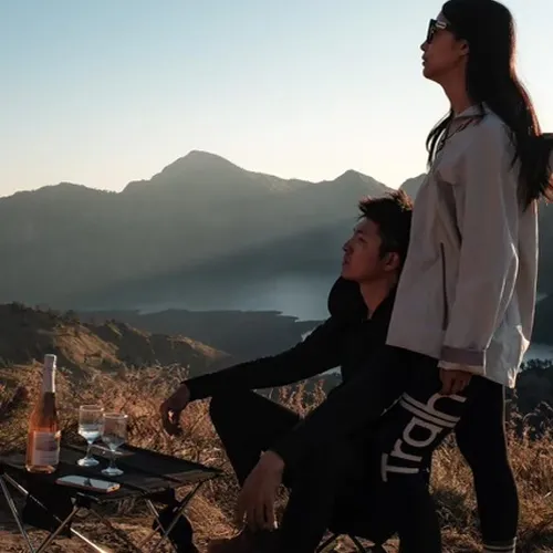 A couple relaxes on a picnic table with a bottle of wine, celebrating their Mount Rinjani hike adventure A couple relaxes on a picnic table with a bottle of wine, celebrating their Mount Rinjani hike adventure