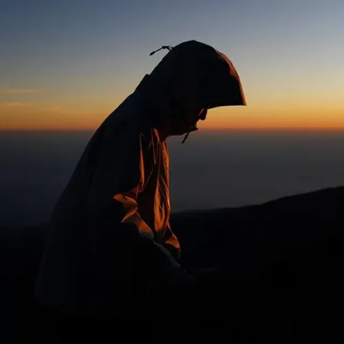 A hiker in a hoodie and jacket stands triumphantly on Mount Rinjani's summit, overlooking the stunning landscape A hiker in a hoodie and jacket stands triumphantly on Mount Rinjani's summit, overlooking the stunning landscape