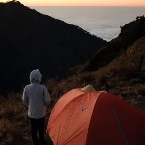 A hiker stands beside a tent on Mount Rinjani, showcasing the stunning mountain landscape during the Sembalun route trek A hiker stands beside a tent on Mount Rinjani, showcasing the stunning mountain landscape during the Sembalun route trek