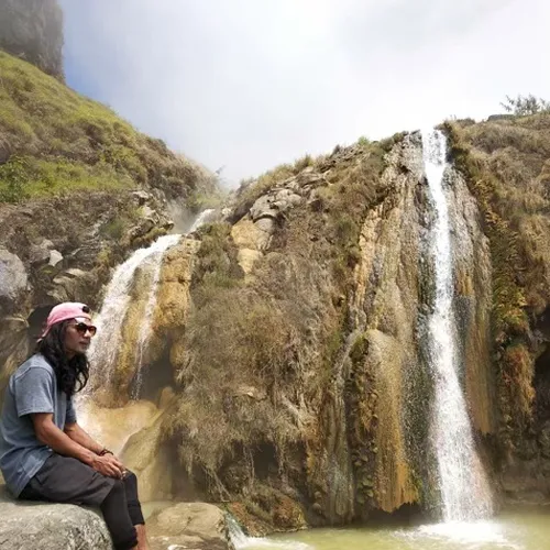 A man relaxes on a rock by a waterfall during a Mount Rinjani hike via the Senaru route A man relaxes on a rock by a waterfall during a Mount Rinjani hike via the Senaru route