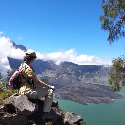 A man sits on a rock, gazing at a serene lake during the Mount Rinjani hike at Crater Rim Senaru A man sits on a rock, gazing at a serene lake during the Mount Rinjani hike at Crater Rim Senaru