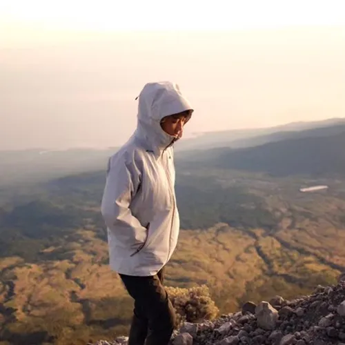 A man wearing a white jacket stands atop Mount Rinjani, celebrating the summit after a challenging hike on the Sembalun route A man wearing a white jacket stands atop Mount Rinjani, celebrating the summit after a challenging hike on the Sembalun route