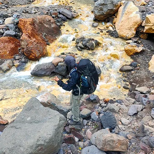 A man with a backpack stands on rocks by a stream, enjoying the scenic view during a Mount Rinjani hike A man with a backpack stands on rocks by a stream, enjoying the scenic view during a Mount Rinjani hike