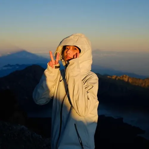 A woman in a white jacket stands on Mount Rinjani's summit, taking in the panoramic views from the hike via Sembalun A woman in a white jacket stands on Mount Rinjani's summit, taking in the panoramic views from the hike via Sembalun