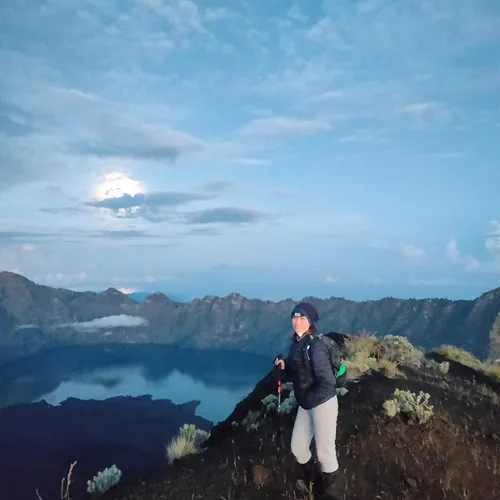 A woman on a mountain peak with a full moon shining brightly behind her, capturing the beauty of Mount Rinjani A woman on a mountain peak with a full moon shining brightly behind her, capturing the beauty of Mount Rinjani