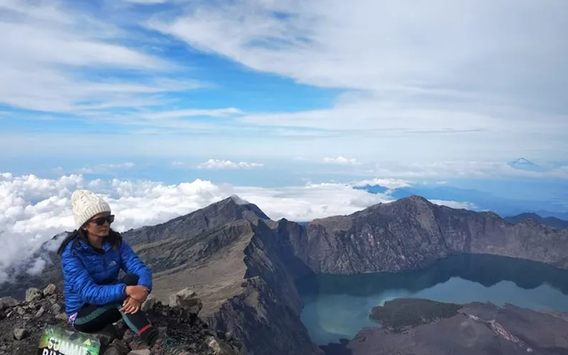A woman sits atop a mountain, overlooking a serene lake, after a 4-day hike on the Senaru route to Mount Rinjani A woman sits atop a mountain, overlooking a serene lake, after a 4-day hike on the Senaru route to Mount Rinjani