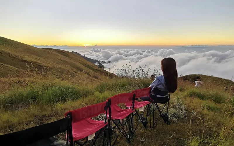 A woman sits on a chair, gazing at the clouds from the Crater Rim Senaru during her Mount Rinjani hike A woman sits on a chair, gazing at the clouds from the Crater Rim Senaru during her Mount Rinjani hike