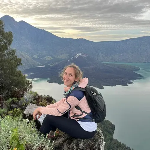 A woman sits on a rock, taking in the stunning lake and mountain scenery on the Mount Rinjani hike A woman sits on a rock, taking in the stunning lake and mountain scenery on the Mount Rinjani hike