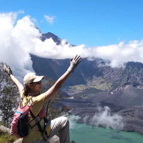At the summit of Mount Rinjani, a woman stands with arms open wide, enjoying the majestic scenery from the Crater Rim Senaru At the summit of Mount Rinjani, a woman stands with arms open wide, enjoying the majestic scenery from the Crater Rim Senaru