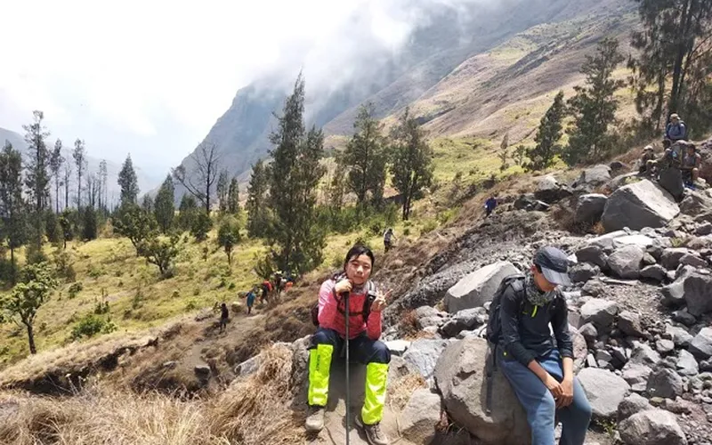 Friends sitting on rocky terrain, enjoying a break during their 4-day Mount Rinjani hike via the Senaru route Friends sitting on rocky terrain, enjoying a break during their 4-day Mount Rinjani hike via the Senaru route