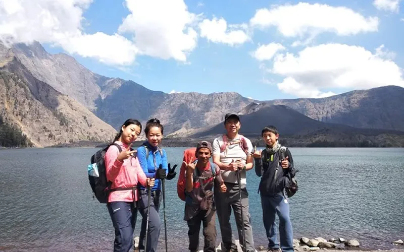 Group of four friends posing for a photo at the summit of Mount Rinjani, overlooking Segara Anak Lake Group of four friends posing for a photo at the summit of Mount Rinjani, overlooking Segara Anak Lake