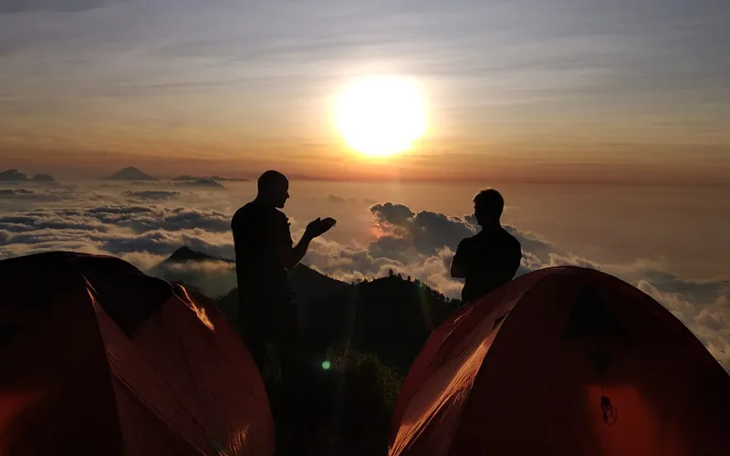 Sunset view of two people by tents, anticipating their Mount Rinjani hike to the summit via the Sembalun route Sunset view of two people by tents, anticipating their Mount Rinjani hike to the summit via the Sembalun route