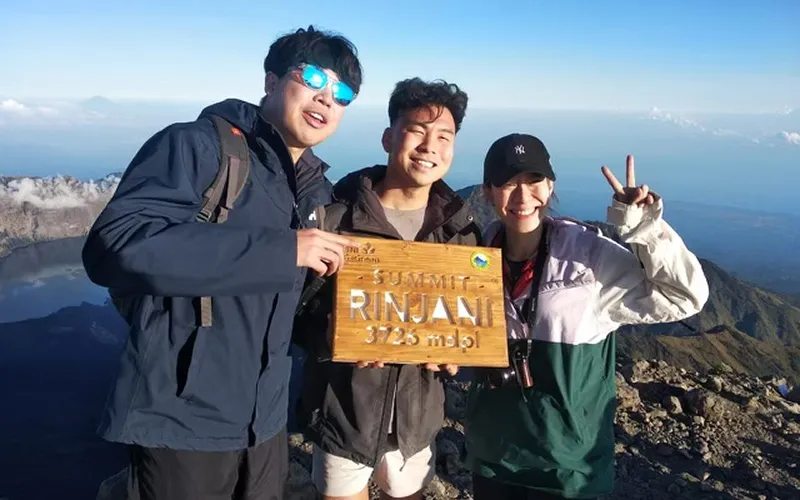 Three friends celebrating at the summit of Mount Rinjani after their hike on the Torean route Three friends celebrating at the summit of Mount Rinjani after their hike on the Torean route