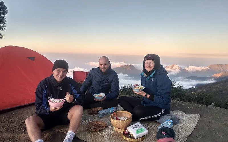 Three hikers enjoy breakfast at a picnic table after reaching the summit of Mount Rinjani Three hikers enjoy breakfast at a picnic table after reaching the summit of Mount Rinjani