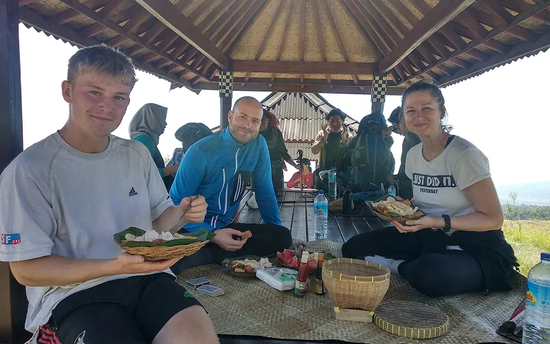 Three hikers on a blanket enjoying lunch during their Mount Rinjani summit break on the Sembalun route Three hikers on a blanket enjoying lunch during their Mount Rinjani summit break on the Sembalun route