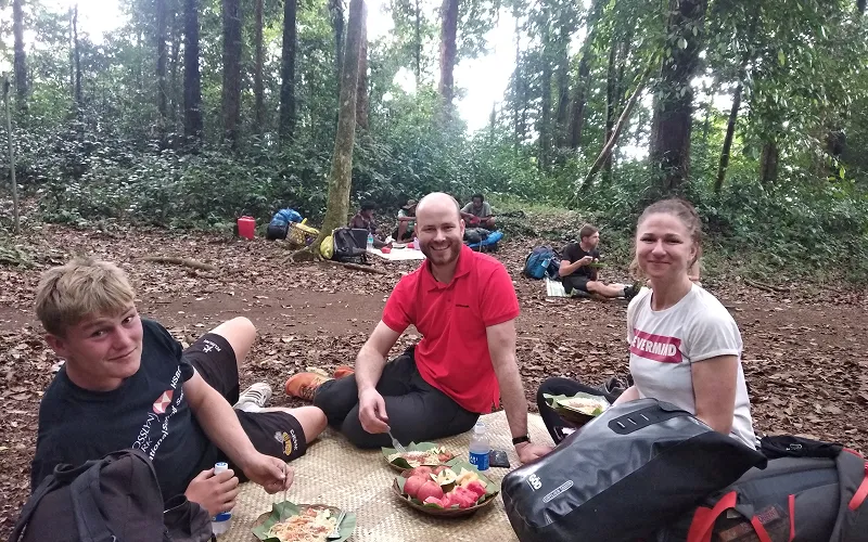 Three hikers resting on the ground in a wooded area during their Mount Rinjani summit trek via the Sembalun route Three hikers resting on the ground in a wooded area during their Mount Rinjani summit trek via the Sembalun route