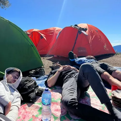 Three hikers resting on the ground near tents after a Mount Rinjani hike via the Senaru route Three hikers resting on the ground near tents after a Mount Rinjani hike via the Senaru route
