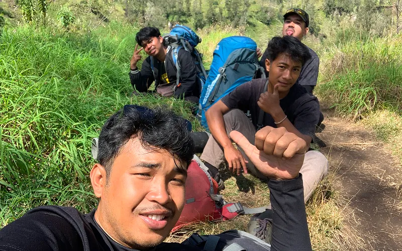 Three men resting on a trail during a Mount Rinjani hike, enjoying the scenic views of the surrounding landscape Three men resting on a trail during a Mount Rinjani hike, enjoying the scenic views of the surrounding landscape