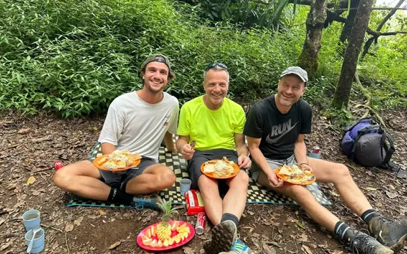 Three men sitting on the ground enjoying plates of food after a Mount Rinjani hike via the Senaru route Three men sitting on the ground enjoying plates of food after a Mount Rinjani hike via the Senaru route