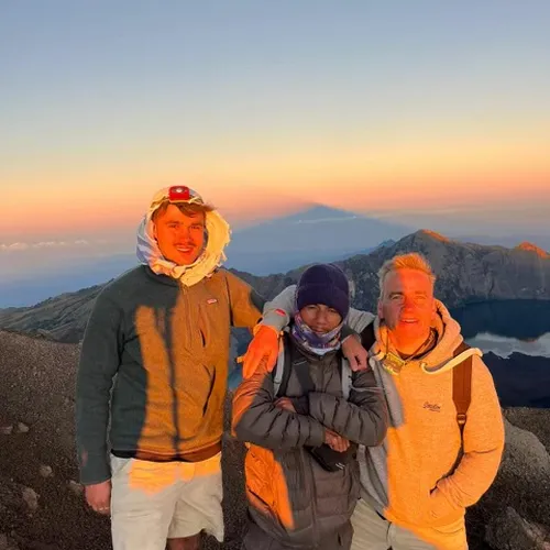 Three men smile for a photo at the summit of Mount Rinjani after their hike via the Sembalun route Three men smile for a photo at the summit of Mount Rinjani after their hike via the Sembalun route
