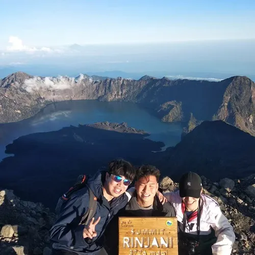 Three people happily posing for a picture atop Mount Rinjani, showcasing the beautiful mountain scenery around them Three people happily posing for a picture atop Mount Rinjani, showcasing the beautiful mountain scenery around them