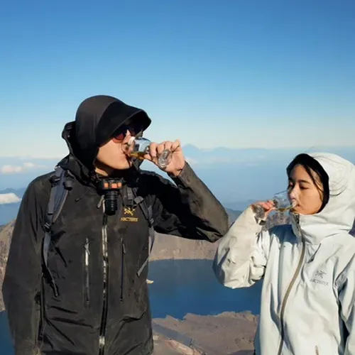 Two friends quenching their thirst with water on top of Mount Rinjani after completing the Sembalun hike Two friends quenching their thirst with water on top of Mount Rinjani after completing the Sembalun hike