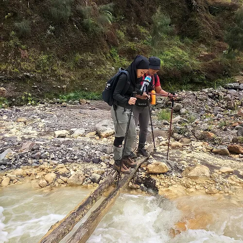 Two hikers crossing a bridge over a river during their Mount Rinjani trek in Torean Two hikers crossing a bridge over a river during their Mount Rinjani trek in Torean