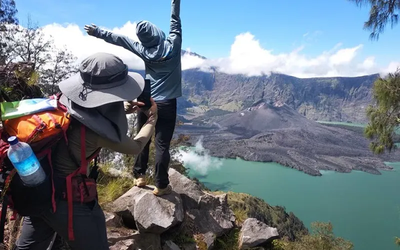 Two hikers on the summit of Mount Rinjani, arms up in excitement, surrounded by the beauty of the crater rim Two hikers on the summit of Mount Rinjani, arms up in excitement, surrounded by the beauty of the crater rim