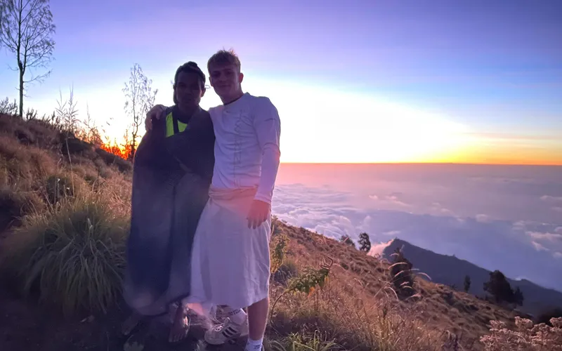 Two hikers stand atop Mount Rinjani at sunset, overlooking the stunning landscape after their summit trek via the Sembalun route Two hikers stand atop Mount Rinjani at sunset, overlooking the stunning landscape after their summit trek via the Sembalun route