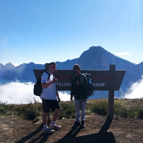 Two individuals stand beside a sign on Mount Rinjani, capturing their hiking experience on the way to Pelawangan Sembalun Two individuals stand beside a sign on Mount Rinjani, capturing their hiking experience on the way to Pelawangan Sembalun