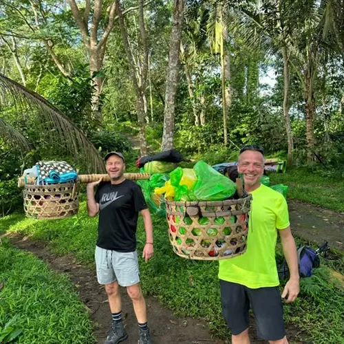 Two men carrying baskets of plastic waste along a trail, participating in a cleanup during their Mount Rinjani hike