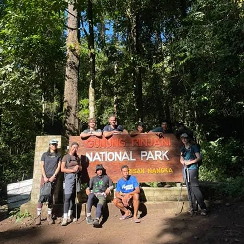 A group of hikers poses in front of the Mount Rinjani National Park sign, marking the start of their trekking adventure A group of hikers poses in front of the Mount Rinjani National Park sign, marking the start of their trekking adventure