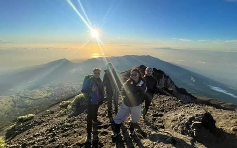 A group of hikers stands triumphantly on Mount Rinjani's summit, overlooking the breathtaking landscape after a 3D2N trek A group of hikers stands triumphantly on Mount Rinjani's summit, overlooking the breathtaking landscape after a 3D2N trek
