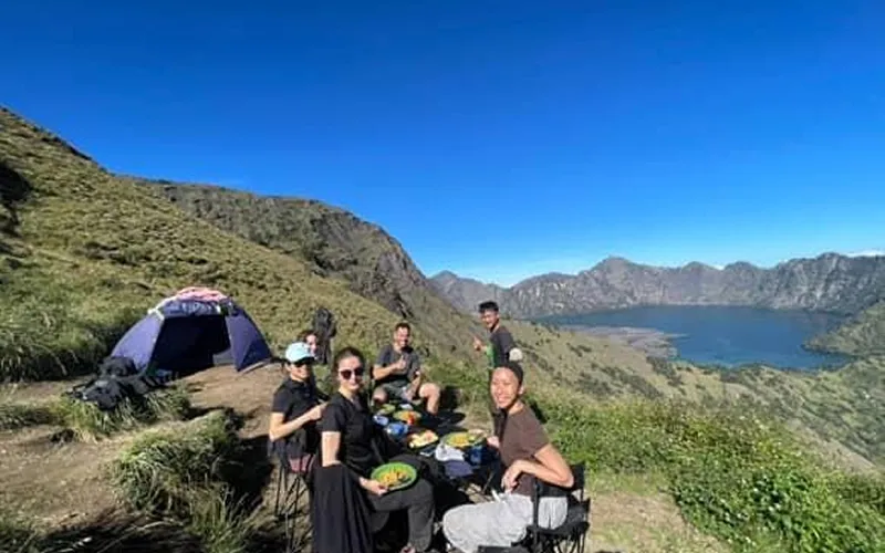 A group of individuals relaxing on a mountain with a tent, part of their 3-day trek at Pelawangan Sembalun campsite A group of individuals relaxing on a mountain with a tent, part of their 3-day trek at Pelawangan Sembalun campsite
