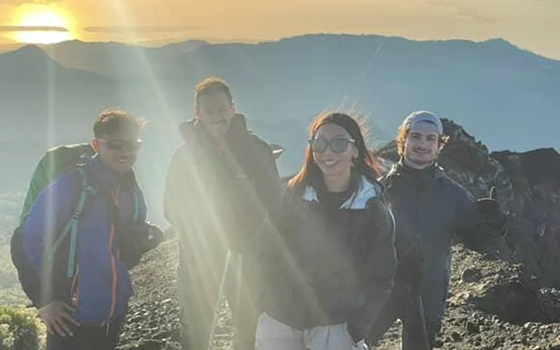 Four people stand atop Mount Rinjani, enjoying the view after completing the Sembalun route trek to the summit Four people stand atop Mount Rinjani, enjoying the view after completing the Sembalun route trek to the summit